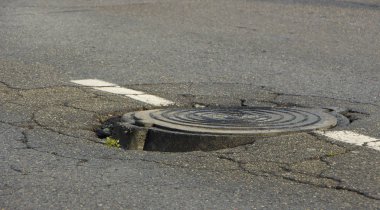Asfalt ve dairesel kanalizasyon kapağı kanalizasyon su kuyusu içinde yol büyük çukur,
