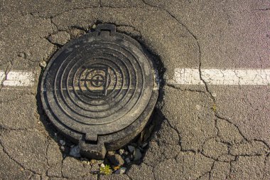 Asfalt ve dairesel kanalizasyon kapağı kanalizasyon su kuyusu içinde yol büyük çukur,