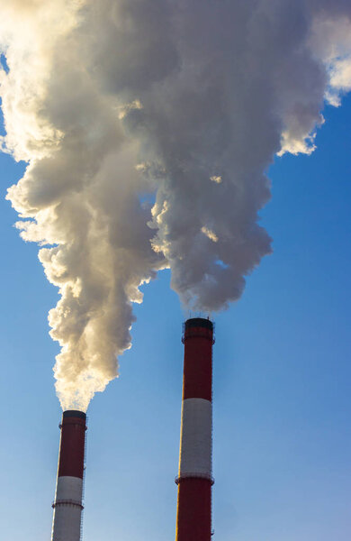 The pipe of the plant emits harmful substances into the atmosphere. Close-up on a sky background