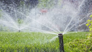 Otomatik fıskiye sistemi yeşil çimlerin arka planında çimleri suluyor