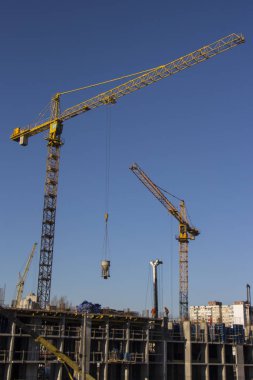 İnşaat vinçleri ve yüksek katlı bina inşaat mavi gökyüzü altında.