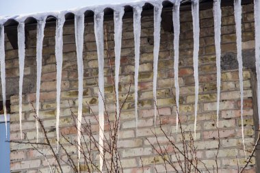 Çatı ve mavi gökyüzünde bulutlar altında eriyen buz sarkıtları