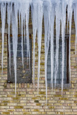 Çatı ve mavi gökyüzünde bulutlar altında eriyen buz sarkıtları