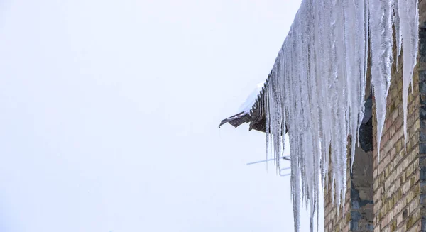 Melting icicles under the roof and clouds in blue sky — Stock Photo, Image