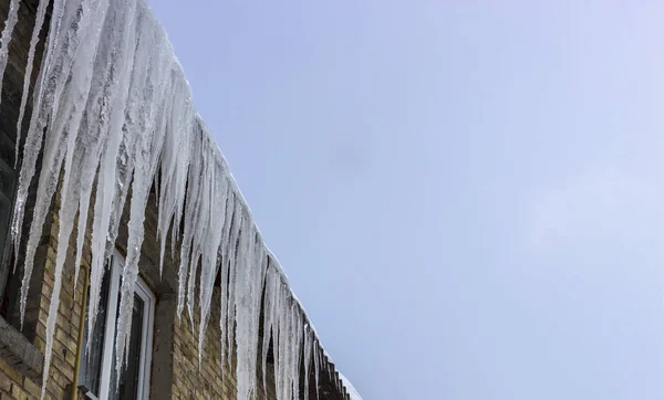 Derretendo icicles sob o telhado e nuvens no céu azul — Fotografia de Stock