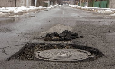 Çukur asfalt yakınındaki sokağın ortasında kanalizasyon kapağı içinde