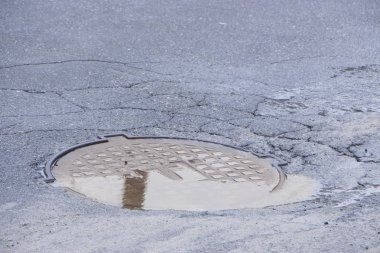 Çukur asfalt yakınındaki sokağın ortasında kanalizasyon kapağı içinde