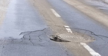 Çukur asfalt yakınındaki sokağın ortasında kanalizasyon kapağı içinde