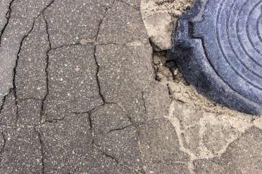 Çukur asfalt yakınındaki sokağın ortasında kanalizasyon kapağı içinde