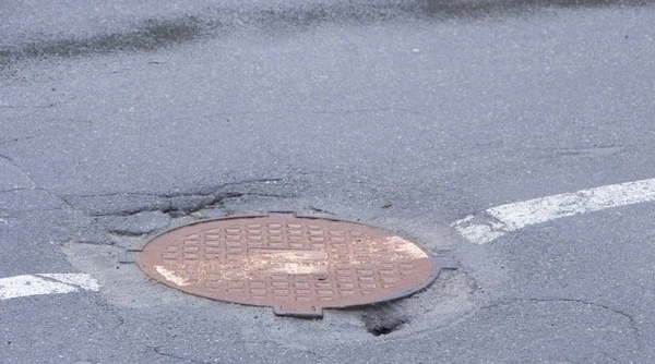 Agujero en asfalto cerca de la escotilla de alcantarillado, en medio de la calle — Foto de Stock