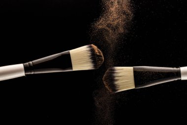 Makyaj anlayışı. İki fırça üreticisi siyah arkaplana toz saçıyor..