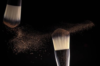 Makyaj anlayışı. İki fırça üreticisi siyah arkaplana toz saçıyor..