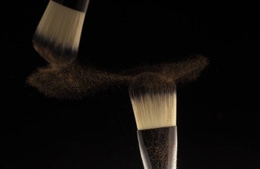 Makyaj anlayışı. İki fırça üreticisi siyah arkaplana toz saçıyor..