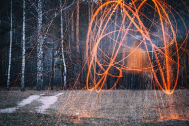 Bir adam sonbahar yaprak döken bir ormanda çelik yünden ya da pamuktan kıvılcımlar yapar. Gizemli arkaplan, yumuşak odak.