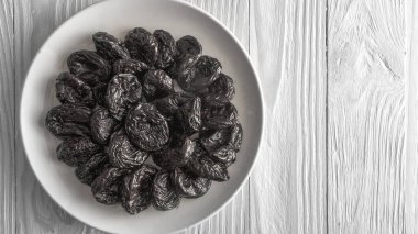 Prunes in a white ceramic plate on a light wooden rustic table.