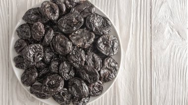 Prunes in a white ceramic plate on a light wooden rustic table.