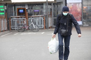 Ukrayna Kiev 23 Mart 2020: Bulutlu bir bahar gününde yüzünde Coronavirus COVID-19 maskesi olan bir adam mağazadan dönüyor.