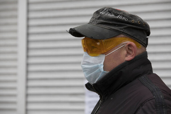 Ukraine Kiev March 23, 2020: A middle-aged man walking outside wearing a goggles mask and hat to protect against COVID-19 coronavirus infection.