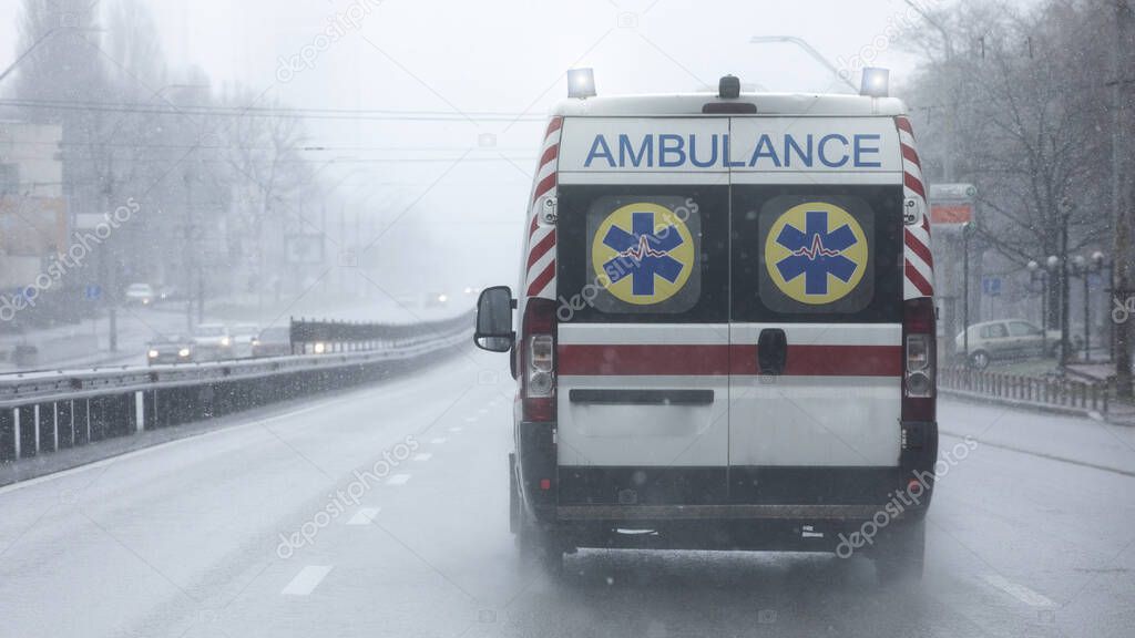 Ambulances with flashing lights on are moving at high speed on the street. Bad weather, rain with sleet.