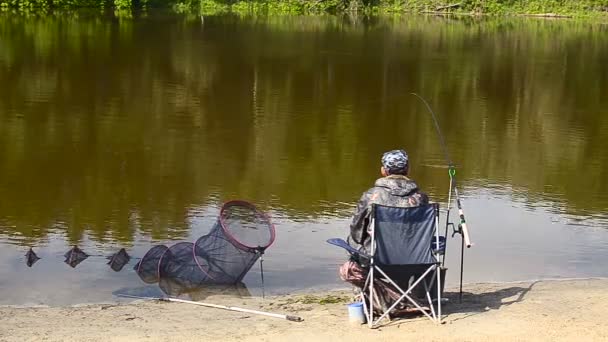 Pescatore uomo sta pescando sulla riva del fiume, il lago sulla mangiatoia affrontare — Video Stock