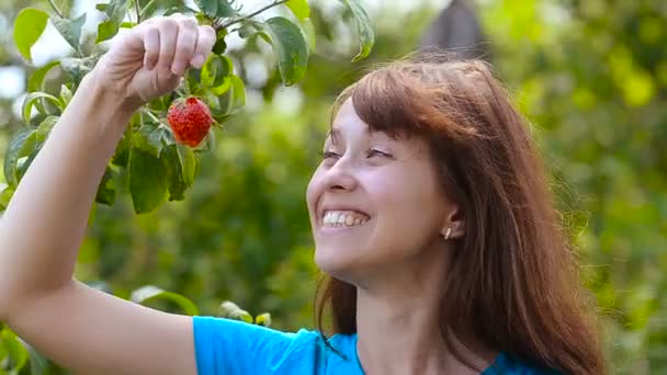 Menina no jardim comer morango vermelho, em um fundo verde , — Vídeo de Stock