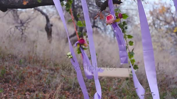 Swing on tree decorated with flowers, blue ribbon with red flowers, wind shakes the beautiful swing — Stock Video