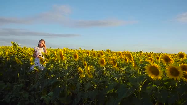 Dospívající dívka mluví po telefonu v barvách žluté slunečnice dívka drží telefon v ruce na poli slunečnice na pozadí modré oblohy. — Stock video