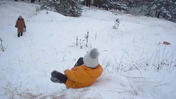 Niño feliz montando con colinas nevadas en el parque de invierno, una chica se ríe en la nieve unas vacaciones familiares de invierno, hermoso paisaje de invierno — Vídeos de Stock