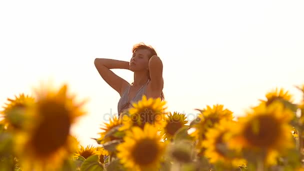 šťastná dívka s vlasy ve větru, chůze v žluté slunečnice, pole zlaté květy, letní slunečný den.