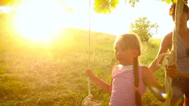 Mom shakes her little girl on swing on a tree in park summer — Stock Video