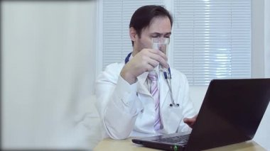bir bardak su, bir dizüstü bilgisayar için ofiste çalışan doktor içme doktor.