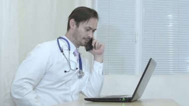 Erkek doktor telefonda, diz üstü bir ofiste çalışan hekim konuşuyor.