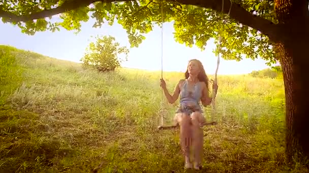 Chica feliz en el sol en columpio en el parque, columpios en el árbol — Vídeos de Stock