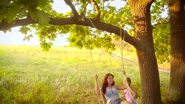 Девушка трясет своей мамой на качелях в парке, качается на дереве — стоковое видео