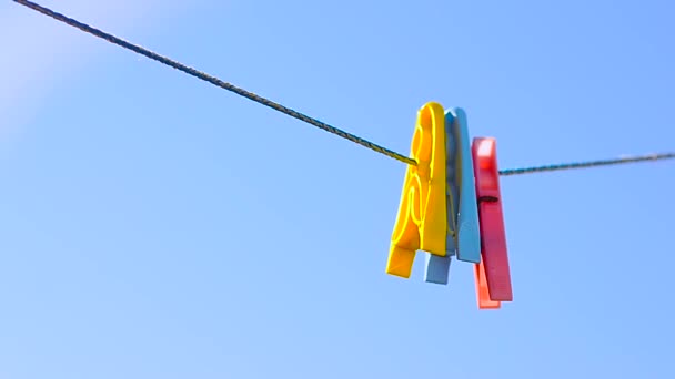 Gekleurde wasknijpers op linnen touw, swing op achtergrond van blauwe hemel. — Stockvideo