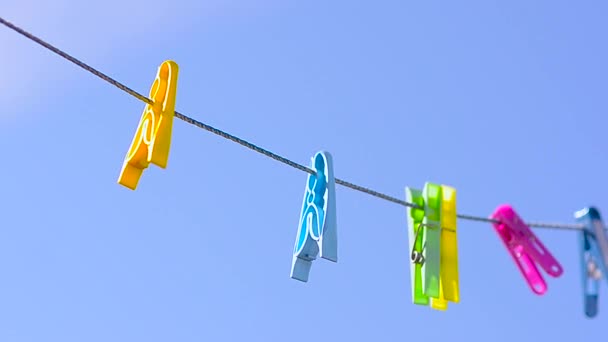 Clothespins colored on linen rope, swing on background of blue sky. — Stock Video