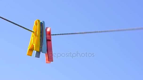 Vêtements colorés chevilles sur corde de lin, balançoire sur fond de ciel bleu . — Video