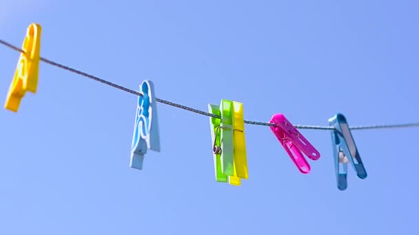 Gekleurde wasknijpers op de waslijn, swingende wind tegen blauwe hemel. — Stockvideo