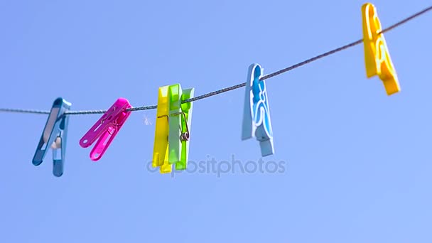 Färgade klädnypor på klädstreck, svängande vind mot blå himmel. — Stockvideo