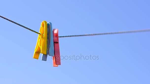 Colored clothes pegs on linen rope, swing on background of blue sky. — Stock Video