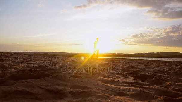 Man står på stranden med boll upplyst av strålar av sol. — Stockvideo