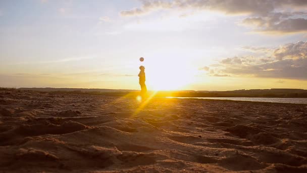 Garçon frappe balle avec sa tête sur la plage au soleil, l'homme d'entraînement avec balle dans le sable le soir d'été . — Video