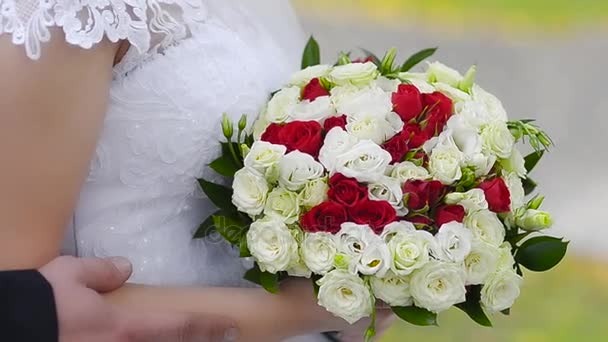 Kytice z červených a bílých růží v rukou nevěsty, dívka v bílé šaty stojí s různobarevné květy v rukou.