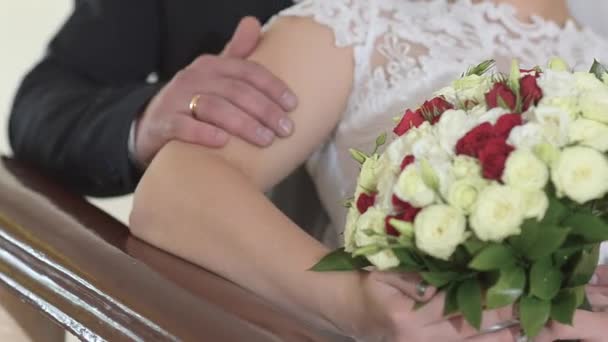 Mani di uomo e donna con un mazzo di fiori di rose rosse e bianche nelle mani della sposa, ragazza in abito bianco seduta con un uomo in abito scuro . — Video Stock