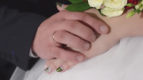 Mãos de homem e mulher com um buquê de flores de rosas vermelhas e brancas nas mãos da noiva, menina de vestido branco sentado com um homem em um terno escuro . — Vídeo de Stock
