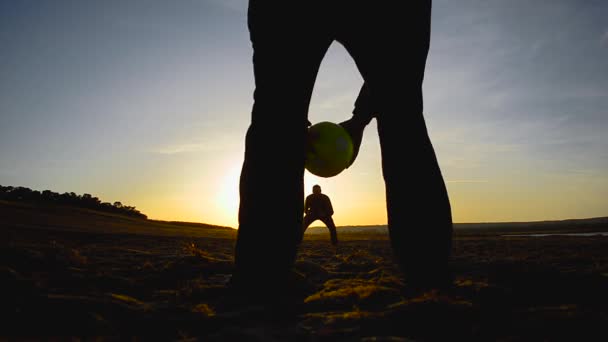 Goleiro pega bola, chuta uma bola de futebol, silhuetas de homens jogando futebol na praia na primavera . — Vídeo de Stock