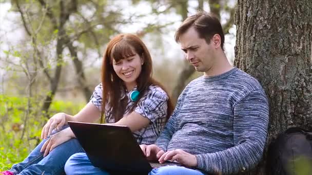 Man en meisje werkt op laptop in park in het voorjaar — Stockvideo