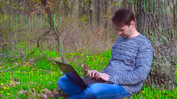 Програміст працює на комп'ютері в парку навесні, зелений цифровий код на відео — стокове відео