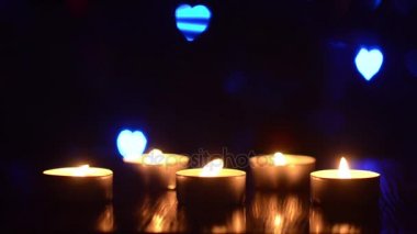 mum alevi sallar Rüzgar, karanlık bir odada, yanıp sönen renkli bokeh kalpler mavi kırmızı yeşil bir masada mumlar yanan.
