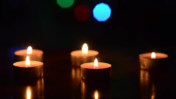 Velas ardientes en una mesa en una habitación oscura, parpadeando corazones bokeh coloridos azul rojo verde, decoración festiva de la habitación . — Vídeo de stock